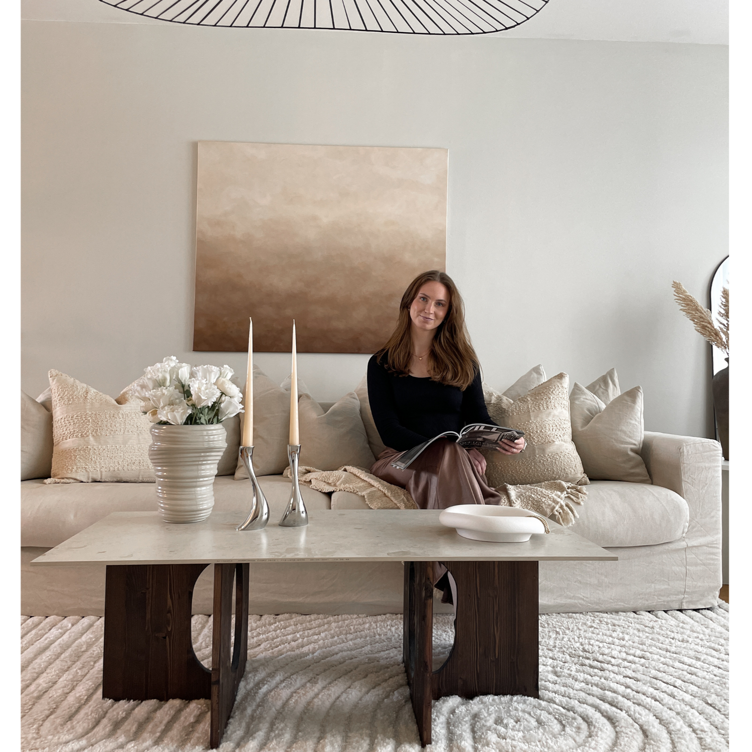 En kvinna som sitter i en beige soffa i ett harmoniskt vardagsrum med en brun och beige tavla på väggen