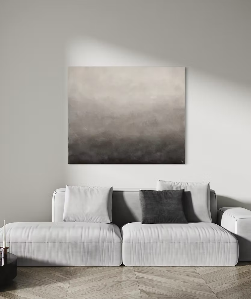 Stillfullt vardagsrum med en stor ljusgrå soffa. På den vita väggen bakom soffan hänger en stor abstrakt målning med mjuka skiftningar i greige