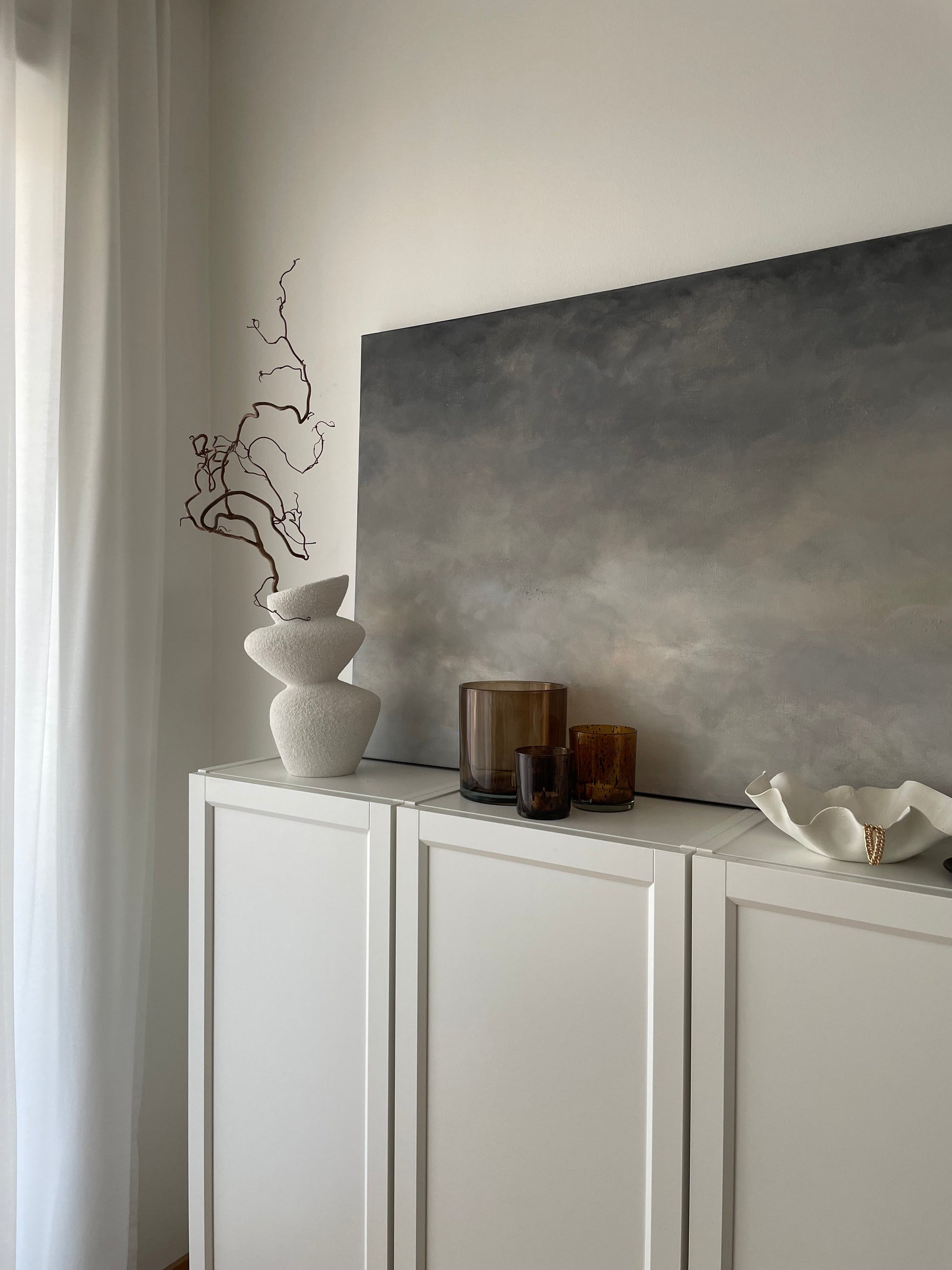 Overcast av Elin Palmgren – abstrakt tavla i grå och beige på en vit skänk i minimalistiskt rum